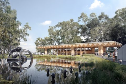 A modern pavilion with a geometric roof stands beside a reflective pond in the Sculpture Garden of the National Gallery of Australia. Sculptures dot the water, surrounded by lush greenery. People are walking and enjoying the serene landscape under a clear blue sky.