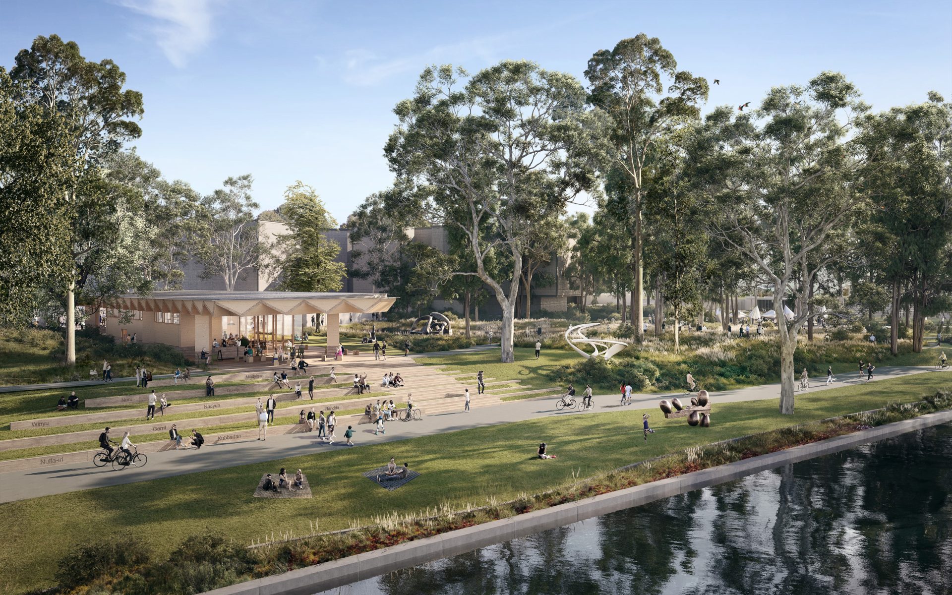 A scenic riverside park features people walking, cycling, and sitting on the grass amidst a sculpture garden reminiscent of a design competition entry. A modern pavilion and playground are surrounded by tall trees. The river flows calmly in the foreground under a clear blue sky.