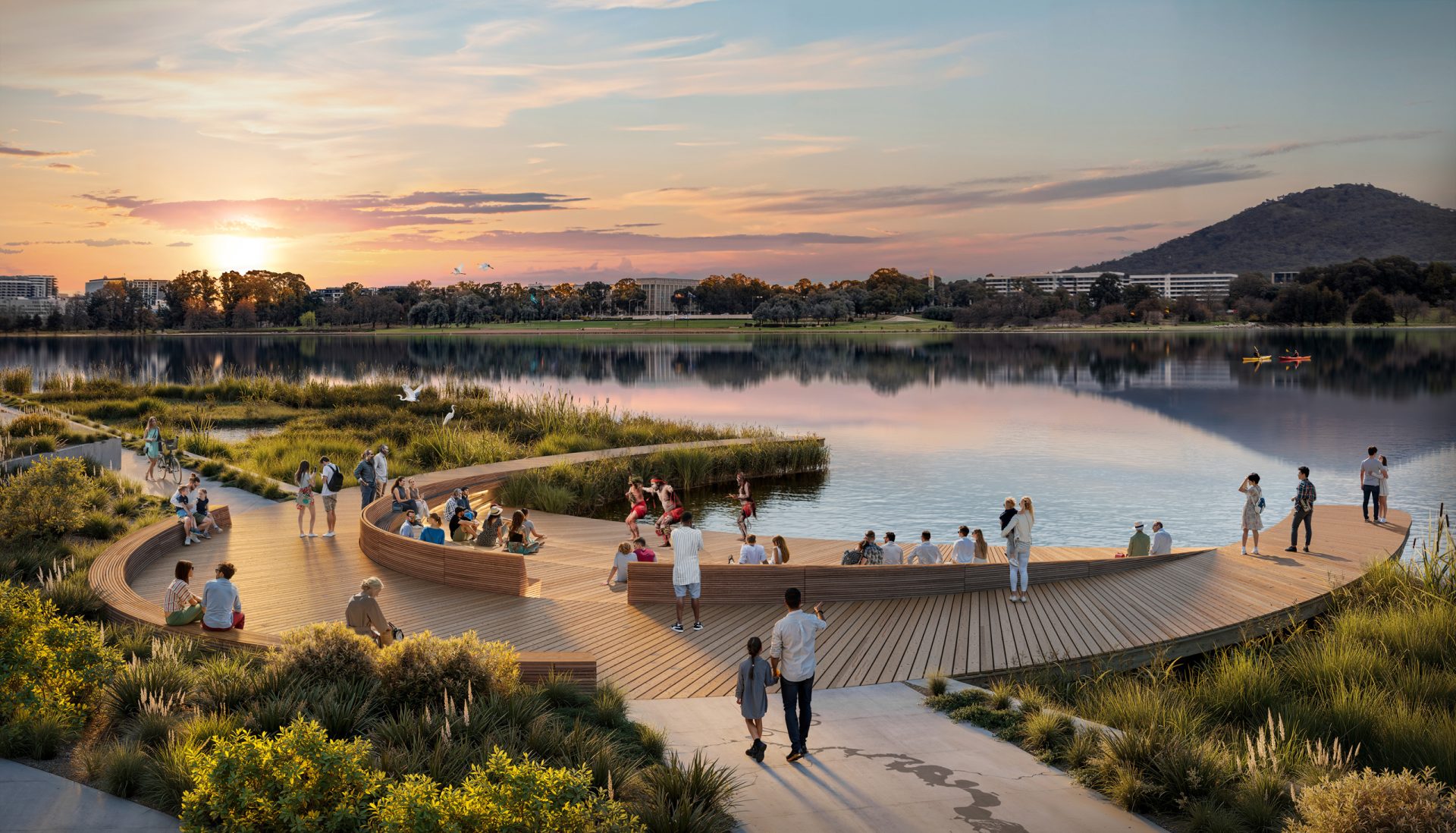 A scenic lakeside view at sunset with a curved wooden boardwalk leads to a charming seating area. Visitors enjoy the surroundings as the landscape unfolds with buildings, trees, and mountains under a colorful sky. Nearby, a sculpture garden awaits art lovers as part of the National Gallery of Australia's collection.