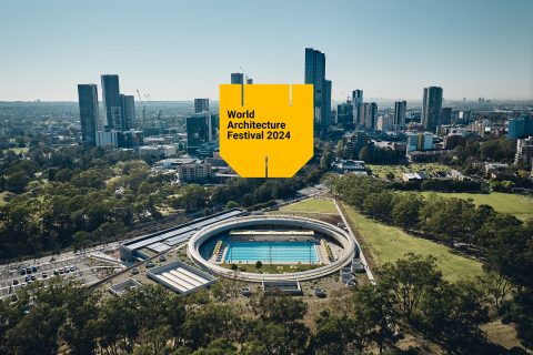 Aerial view of the circular Parramatta Aquatic Centre with a swimming pool, surrounded by trees and urban high-rises. A large yellow banner featuring "World Architecture Festival 2024" hovers above, celebrating the World Architecture Prize amid the vibrant cityscape.